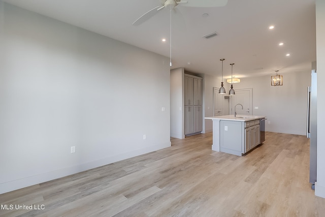 kitchen with a center island with sink, light hardwood / wood-style flooring, pendant lighting, gray cabinetry, and sink