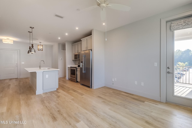 kitchen featuring appliances with stainless steel finishes, sink, hanging light fixtures, light hardwood / wood-style floors, and a kitchen island with sink