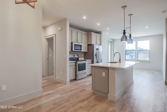 kitchen featuring appliances with stainless steel finishes, sink, pendant lighting, light hardwood / wood-style flooring, and a kitchen island with sink