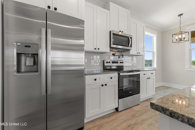 kitchen with light wood-type flooring, appliances with stainless steel finishes, tasteful backsplash, a notable chandelier, and white cabinetry