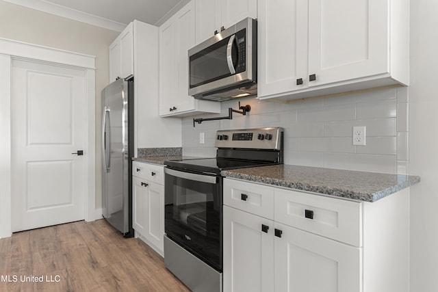 kitchen with dark stone counters, white cabinets, light wood-type flooring, appliances with stainless steel finishes, and tasteful backsplash