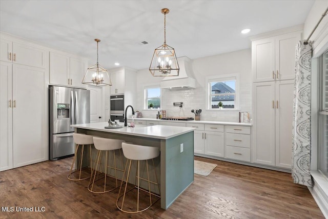 kitchen featuring stainless steel appliances, a notable chandelier, white cabinets, premium range hood, and tasteful backsplash