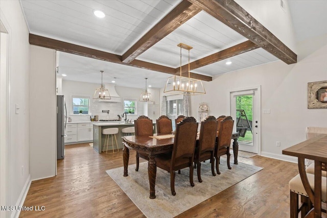 dining space with light wood finished floors, an inviting chandelier, beam ceiling, and plenty of natural light