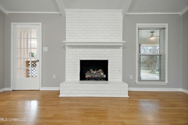 unfurnished living room featuring light wood-type flooring, a brick fireplace, beamed ceiling, and a textured ceiling