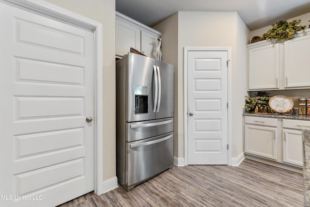 kitchen with stone counters, stainless steel fridge, white cabinets, baseboards, and light wood-style floors