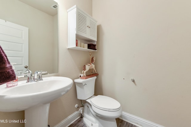 half bathroom featuring a sink, toilet, baseboards, and wood finished floors