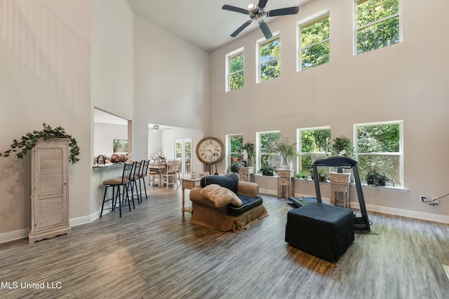living area featuring wood finished floors, plenty of natural light, baseboards, a towering ceiling, and ceiling fan