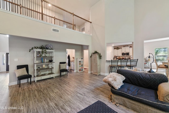 living area with visible vents, wood finished floors, baseboards, and a high ceiling
