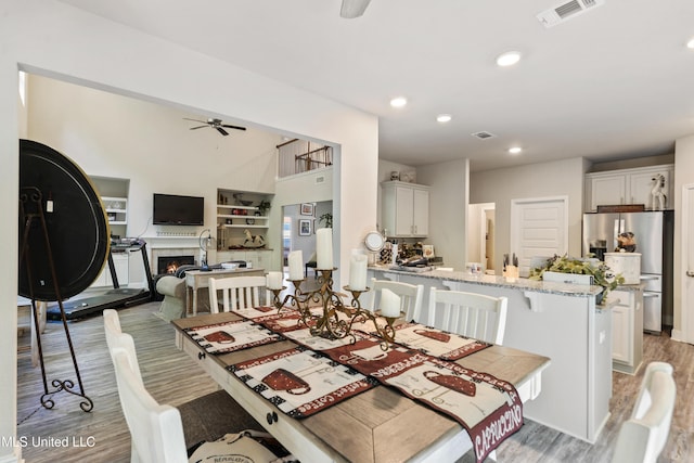 dining space with a ceiling fan, a warm lit fireplace, recessed lighting, visible vents, and light wood-type flooring