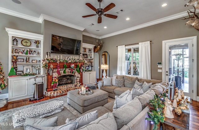 living room featuring hardwood / wood-style flooring, ceiling fan, crown molding, and a fireplace