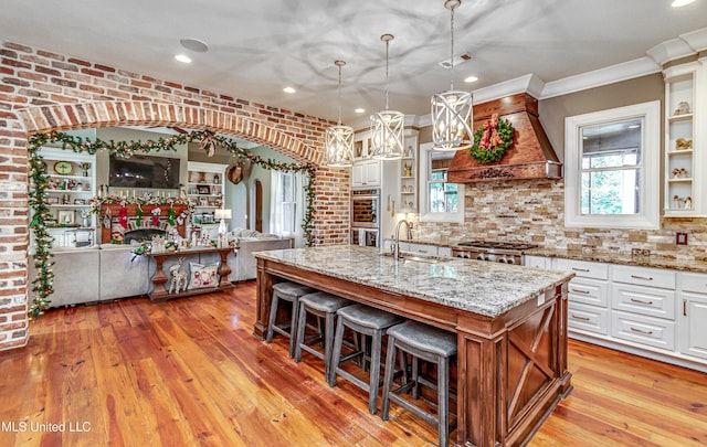 kitchen featuring white cabinets, decorative light fixtures, sink, and an island with sink