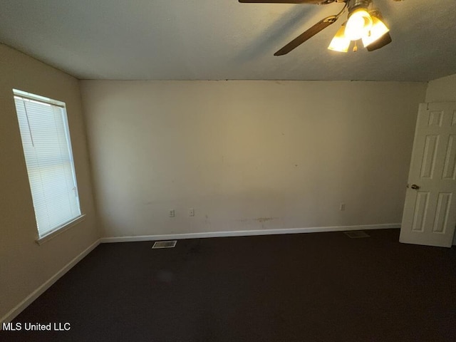 spare room featuring a ceiling fan, dark carpet, visible vents, and baseboards