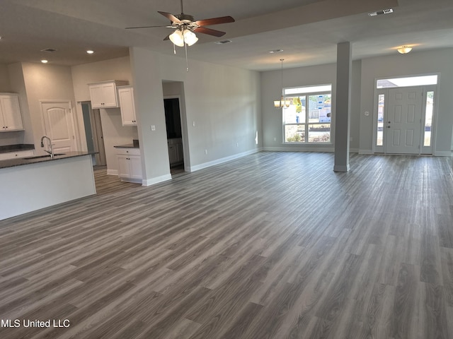 unfurnished living room featuring ceiling fan with notable chandelier, sink, and dark wood-type flooring