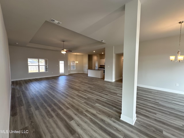 unfurnished living room featuring a raised ceiling, dark hardwood / wood-style floors, and ceiling fan with notable chandelier