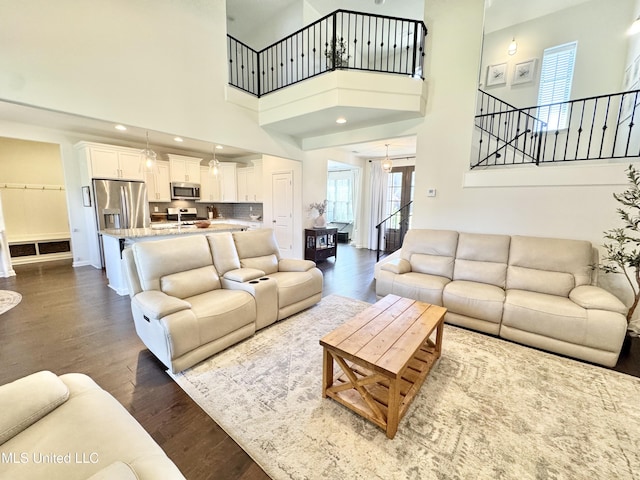 living area featuring dark wood finished floors, stairway, baseboards, a towering ceiling, and recessed lighting