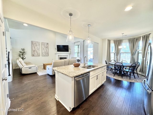kitchen with a sink, stainless steel appliances, a fireplace, open floor plan, and light stone countertops