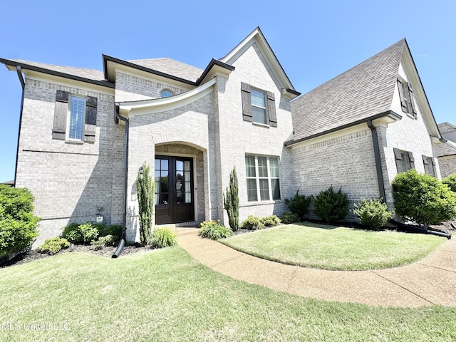 french country home featuring a front yard, brick siding, and french doors