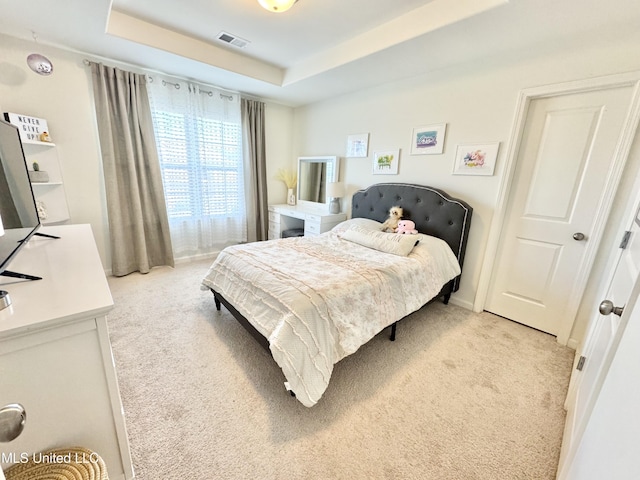 bedroom featuring a tray ceiling, light carpet, and visible vents