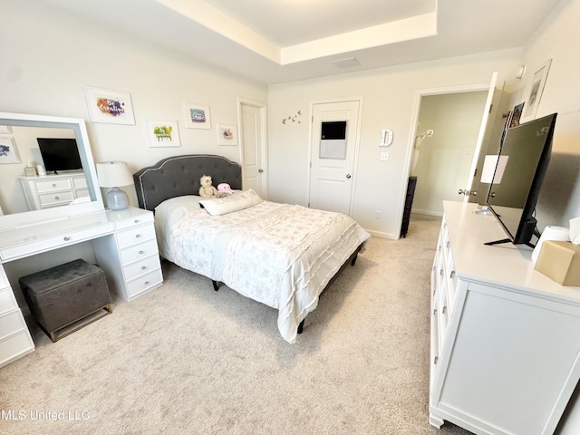 bedroom with a tray ceiling, light carpet, and visible vents