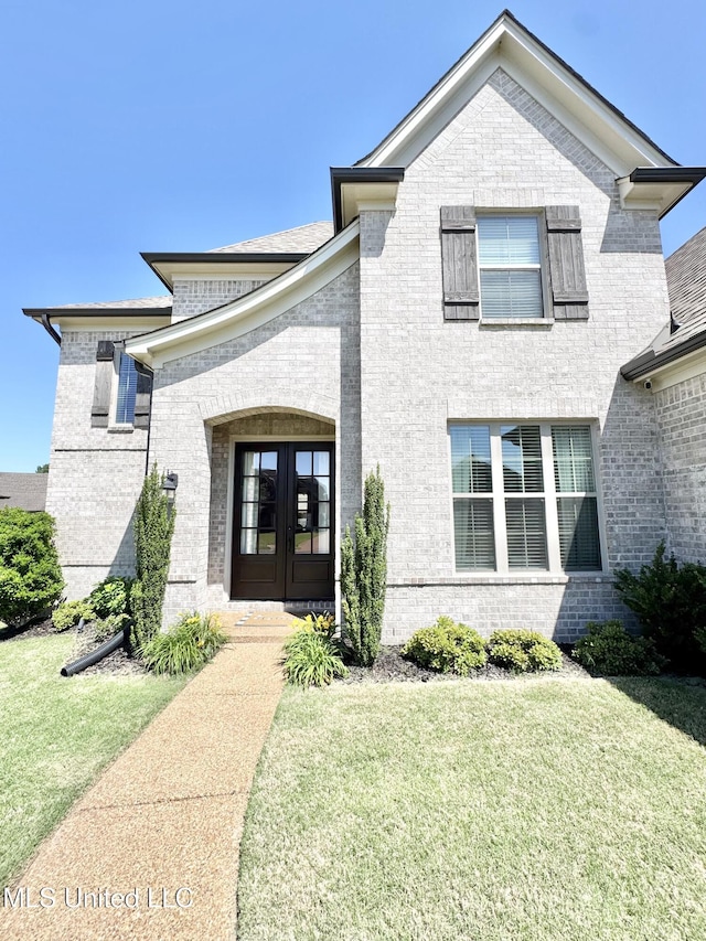 french country inspired facade featuring brick siding, french doors, and a front lawn