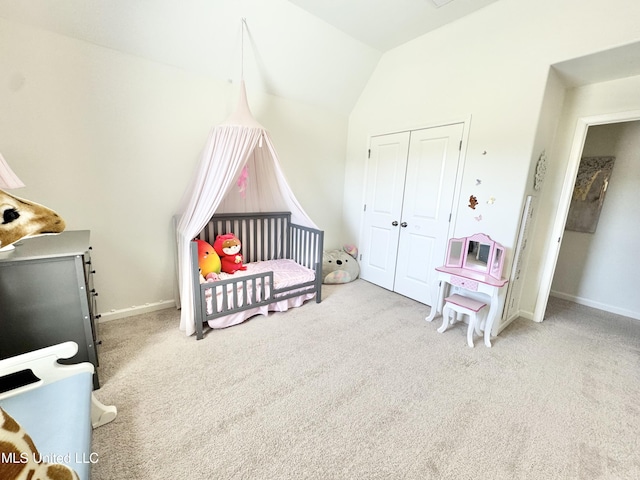 carpeted bedroom with lofted ceiling, a closet, baseboards, and a crib