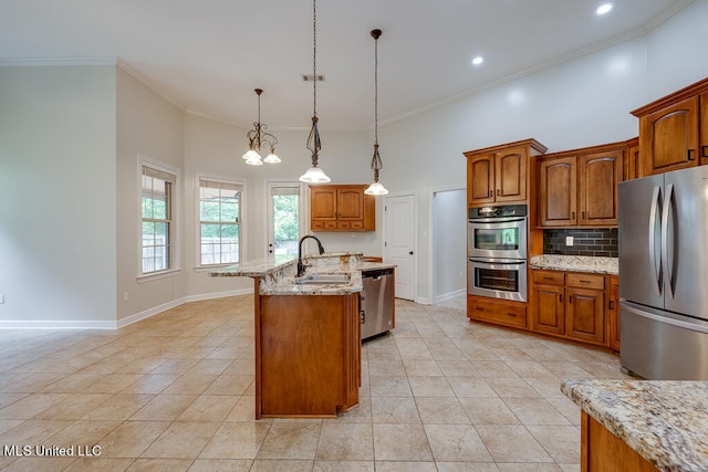 kitchen featuring a kitchen island with sink, hanging light fixtures, sink, light stone countertops, and appliances with stainless steel finishes