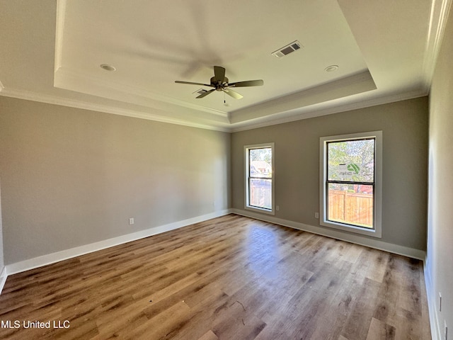 empty room featuring light wood-type flooring, ceiling fan, crown molding, and a tray ceiling