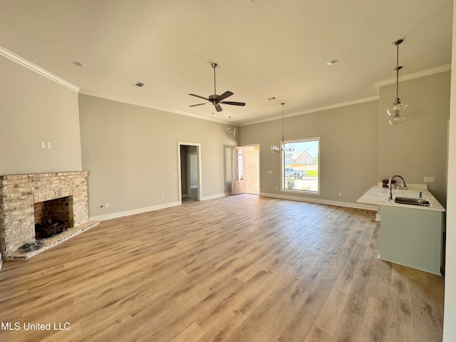 unfurnished living room featuring a fireplace, sink, ornamental molding, light wood-type flooring, and ceiling fan