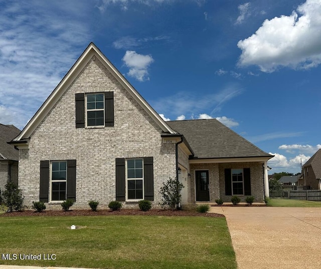 view of front of home featuring a shingled roof, a front yard, and brick siding