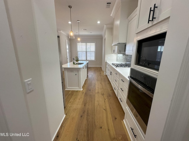 kitchen featuring appliances with stainless steel finishes, white cabinets, a kitchen island with sink, and pendant lighting