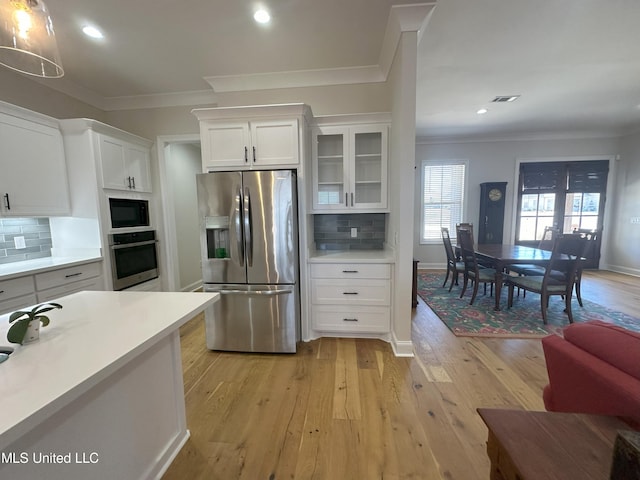 kitchen with light hardwood / wood-style flooring, crown molding, white cabinetry, appliances with stainless steel finishes, and tasteful backsplash