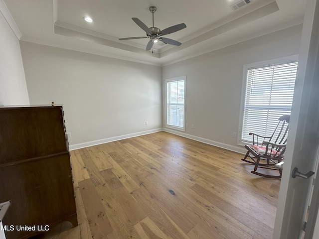 empty room featuring a wealth of natural light, crown molding, light hardwood / wood-style flooring, and a raised ceiling