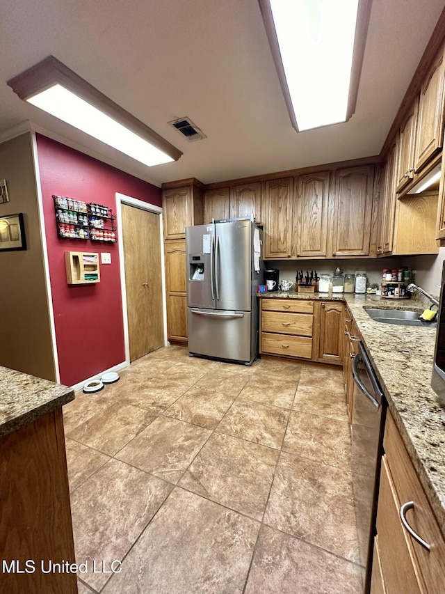 kitchen featuring light stone countertops, dishwasher, brown cabinetry, stainless steel refrigerator with ice dispenser, and visible vents