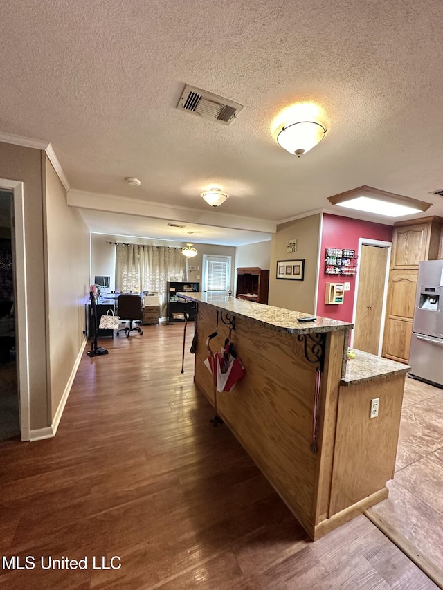 interior space with visible vents, ornamental molding, wood finished floors, stainless steel fridge, and a textured ceiling