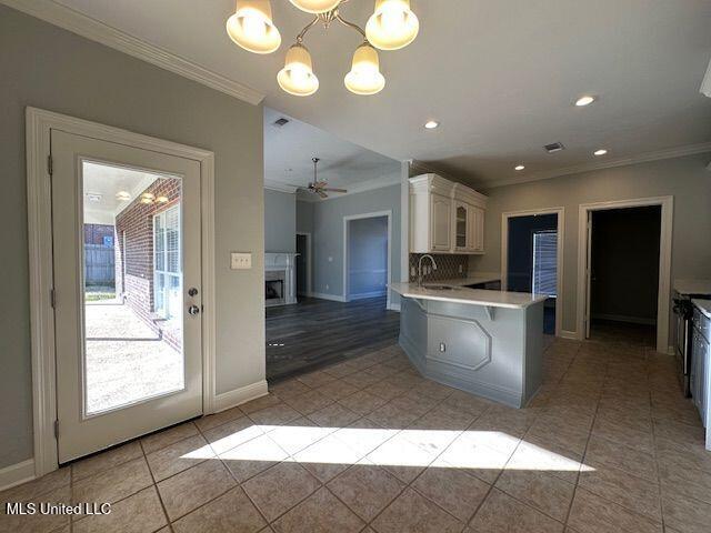 kitchen featuring crown molding, decorative light fixtures, light tile patterned floors, kitchen peninsula, and a fireplace