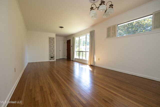 unfurnished room featuring an inviting chandelier, crown molding, and dark hardwood / wood-style flooring