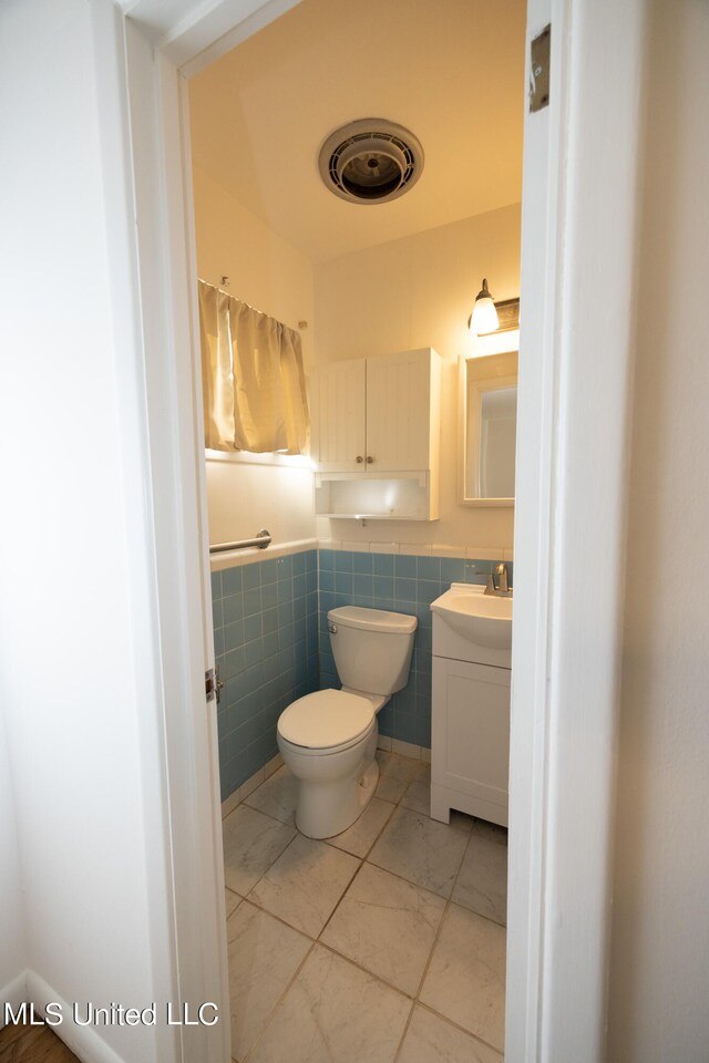 bathroom featuring toilet, vanity, and tile walls