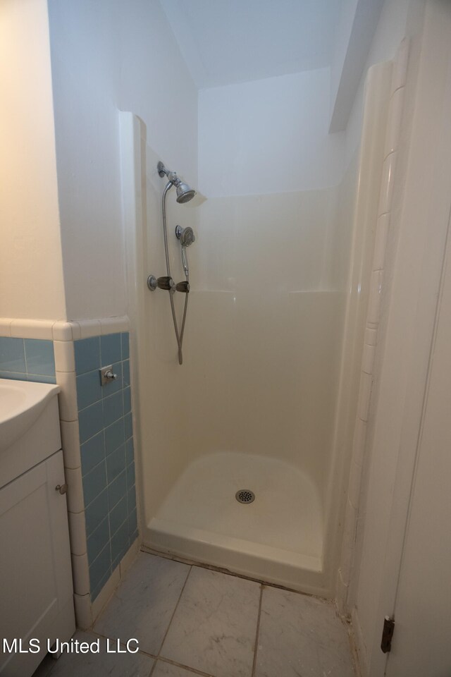 bathroom featuring vanity, tile patterned floors, a shower, and tile walls