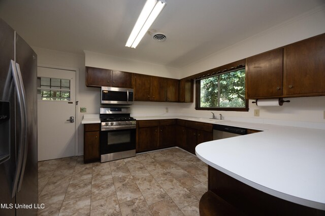 kitchen with kitchen peninsula, dark brown cabinets, appliances with stainless steel finishes, crown molding, and sink