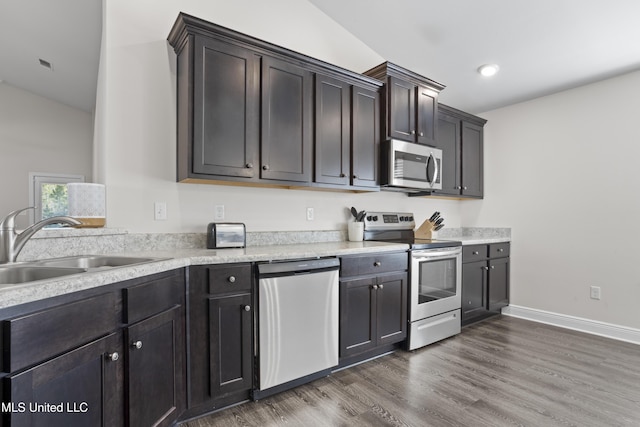 kitchen with a sink, appliances with stainless steel finishes, light countertops, baseboards, and dark wood-style flooring