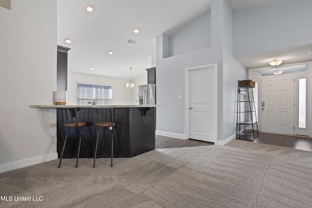 kitchen featuring stainless steel fridge, a kitchen bar, baseboards, and dark colored carpet