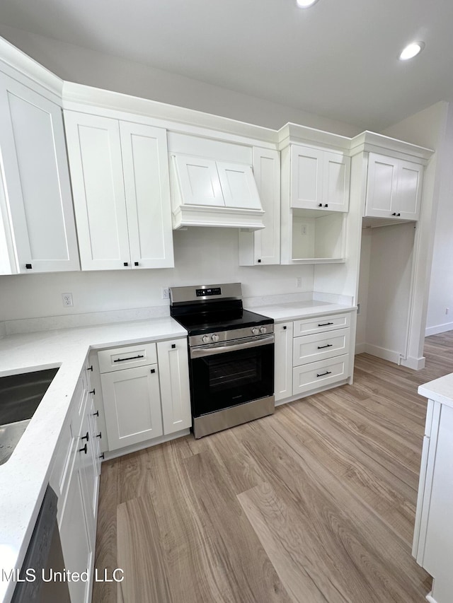 kitchen featuring custom exhaust hood, stainless steel electric range oven, white cabinets, and light wood-type flooring