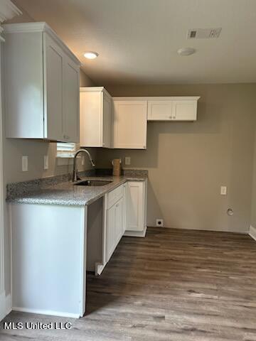 kitchen with stone counters, hardwood / wood-style flooring, sink, and white cabinets