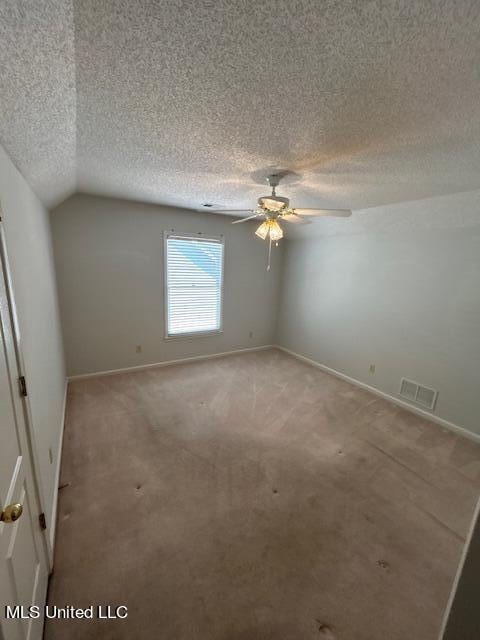 spare room featuring light carpet, a textured ceiling, vaulted ceiling, and ceiling fan