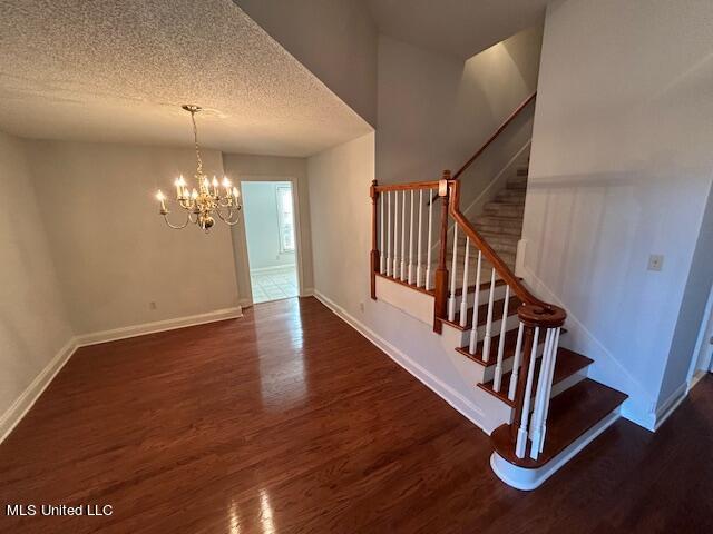 staircase with a notable chandelier, a textured ceiling, and wood-type flooring