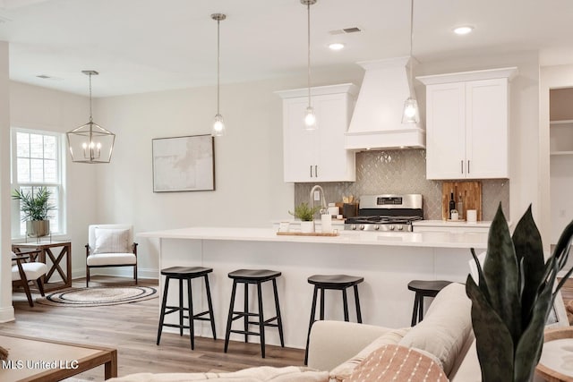 kitchen featuring a breakfast bar, white cabinetry, stainless steel range, custom exhaust hood, and light wood-type flooring