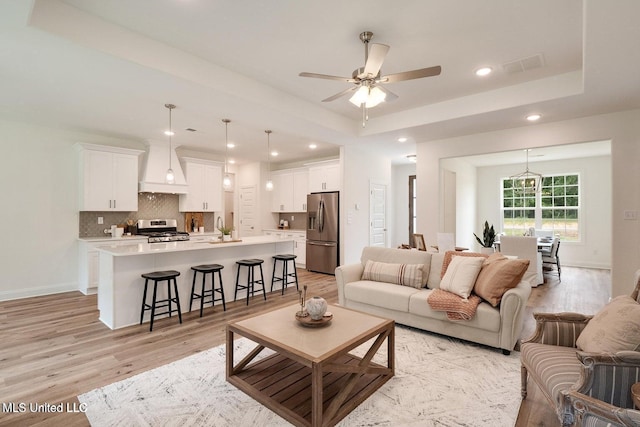 living room with sink, light hardwood / wood-style flooring, a raised ceiling, and ceiling fan