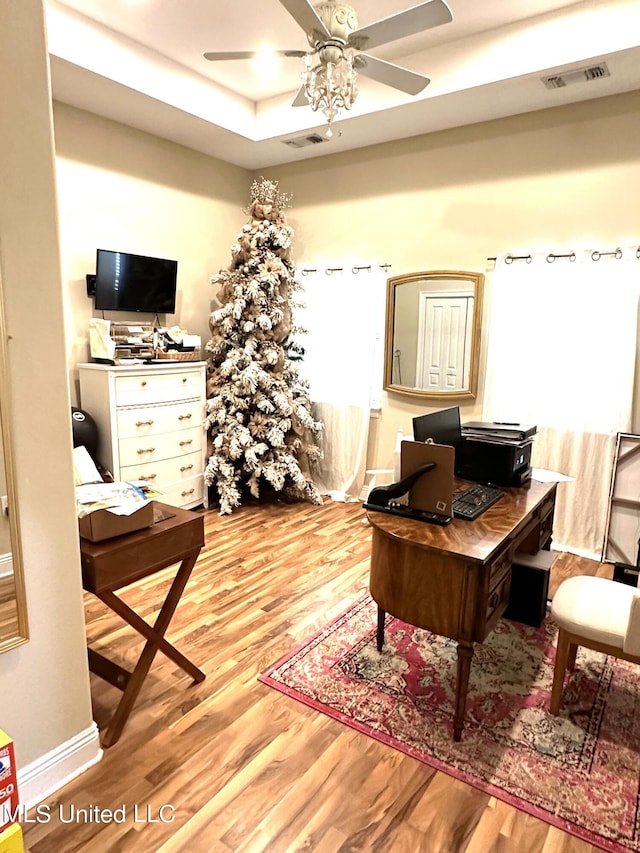 office space featuring ceiling fan, light wood-type flooring, and a tray ceiling