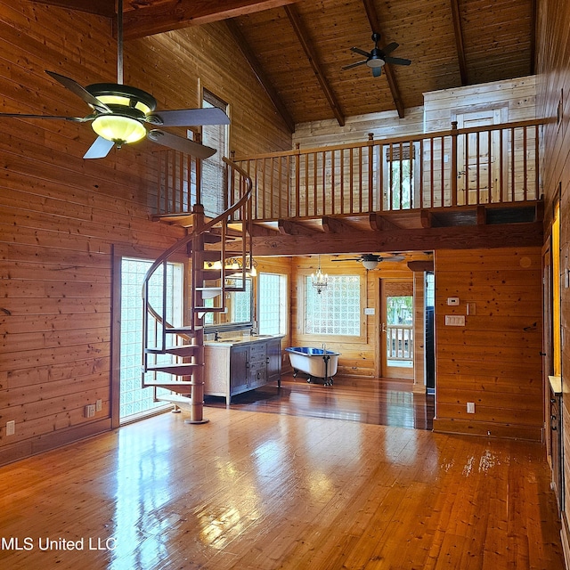 unfurnished living room with beamed ceiling, hardwood / wood-style floors, high vaulted ceiling, and wooden walls