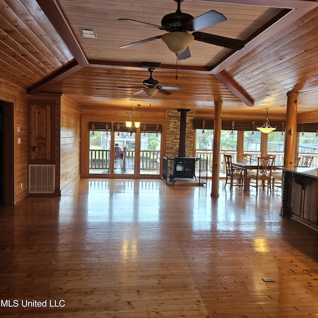 unfurnished living room with lofted ceiling with beams, hardwood / wood-style flooring, a wood stove, and plenty of natural light